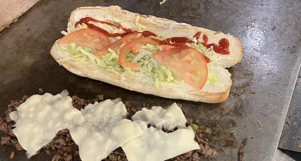 Hero roll with lettuce and tomato next to chopped steak and cheese on the grill